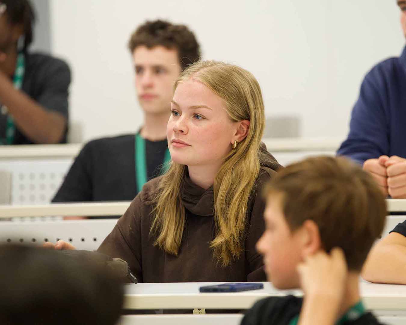 Une élève écoute attentivement pendant un cours, avec d’autres participants en arrière-plan dans un environnement d’apprentissage en groupe.